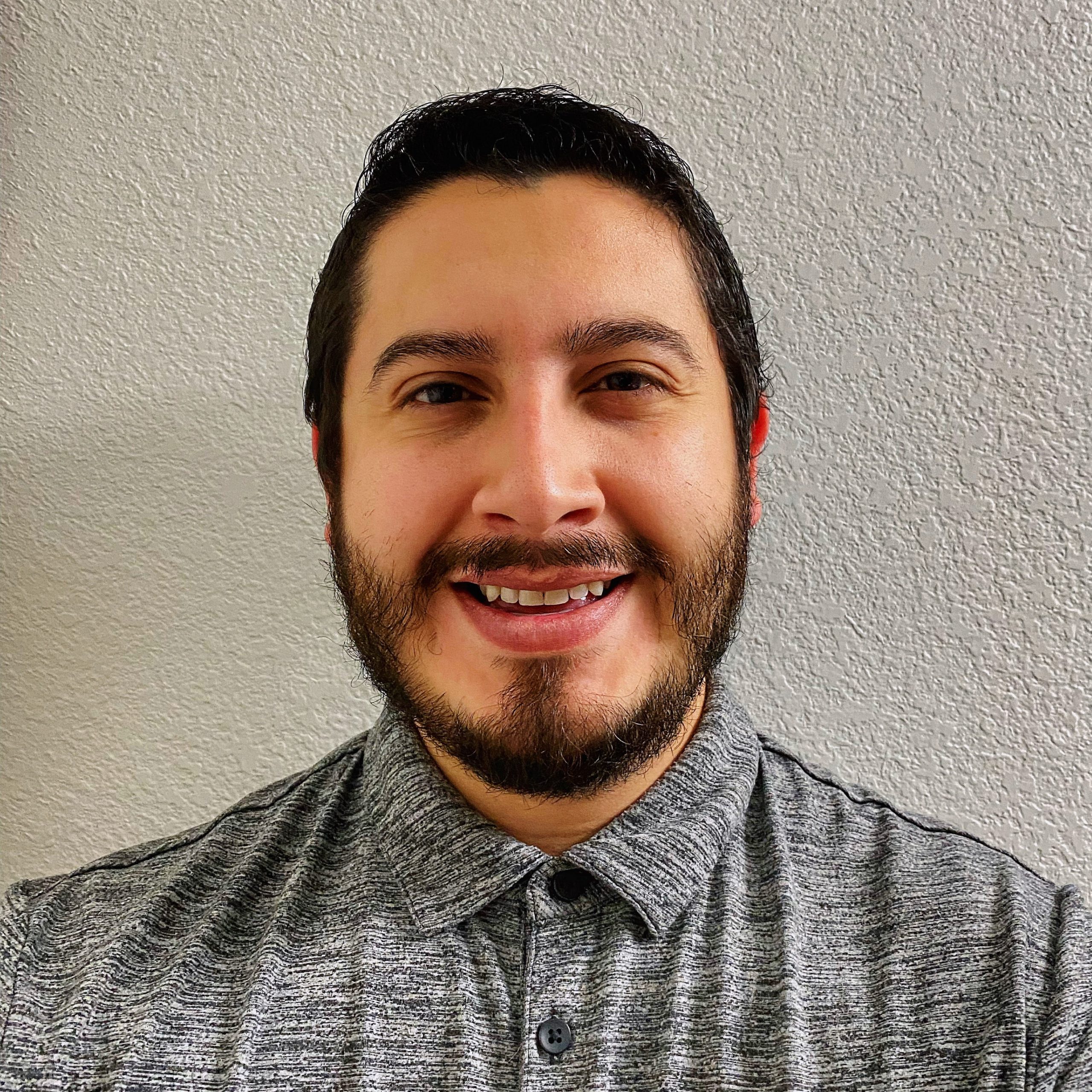 Photo of AT Coordinator Jesse Armijo smiling wearing a gray top in front of a white wall